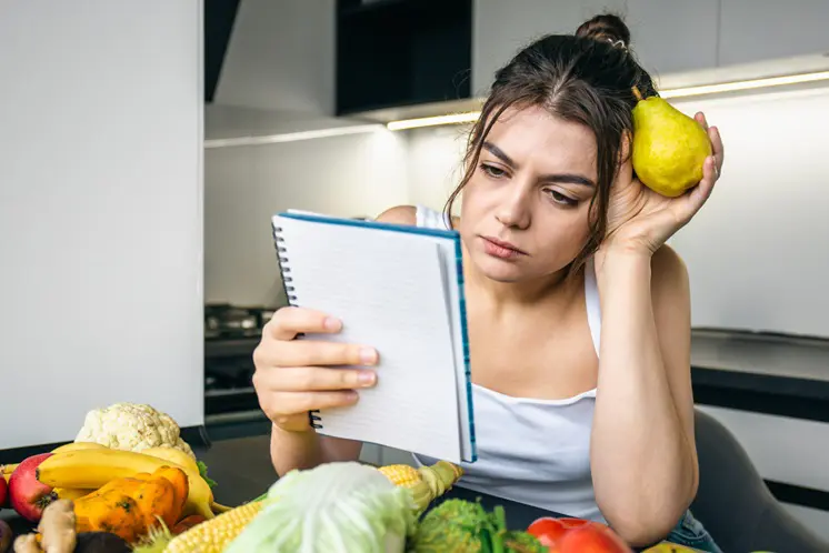 imagem de mulher branca com uma fruta na máo e com duvidas sobre a dieta